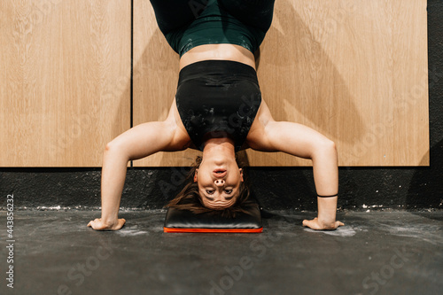 Canvas Print Young woman training on floor in a gym practicing handstand walk