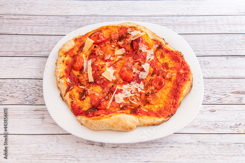 Small wheat thin crust pizza with cherry tomatoes, Parmesan cheese and barbecue sauce on a white plate