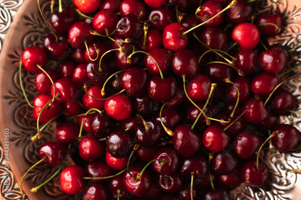 a lot of ripe cherries are lying on a copper tray with a pattern. a lot of ripe cherries are lying on a copper tray with a pattern.