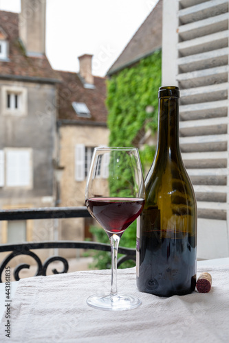 Tasting of burgundy red wine from grand cru pinot noir  vineyards, glass and bottle of wine and view on old town street in Burgundy wine region, France photo