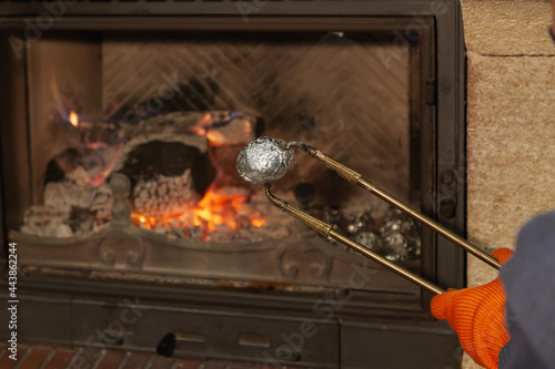Hand holds potatoes in foil with fireplace tongs