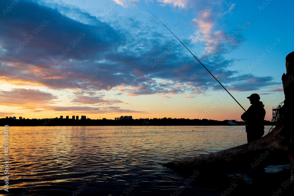 fisherman fishing in the river at sunset against the background of the city silhouette