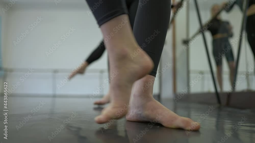 Close-up barefoot legs of female ballet dancer moving in slow motion. Unrecognizable Caucasian young woman rehearsing in dance studio with people dancing at background Close-up barefoot legs of female ballet dancer moving in slow motion. Unrecognizable Caucasian young woman rehearsing in dance studio with people dancing at background