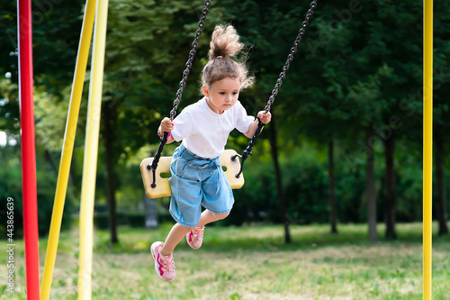 Little pretty girl, cute kid, child is swinging on a swing at summer sunny weather in a park, playing in the children playground