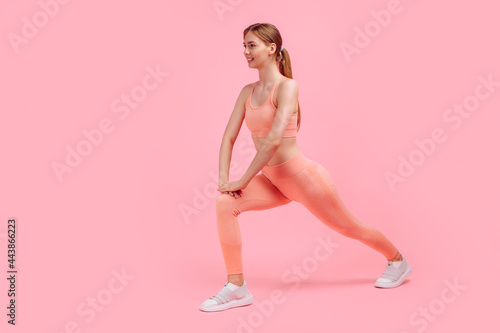 attractive athletic woman in pink tracksuit doing gymnastics and stretching legs isolated on pink background