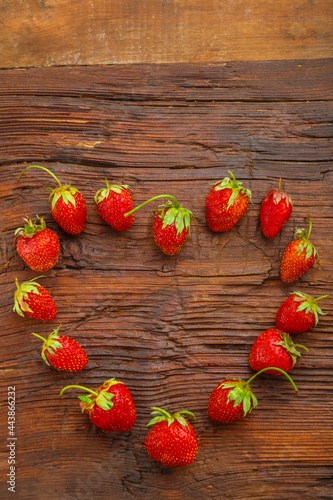 Fresh large strawberries laid out in the shape of a heart on a wooden table.