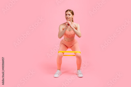 Strong young woman doing exercises with elastic band, Sportswoman doing workout with resistance band, on pink background