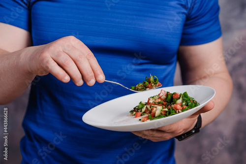Salad with cucumber, tomato and green onions on a plate. A man holding a plate of salad