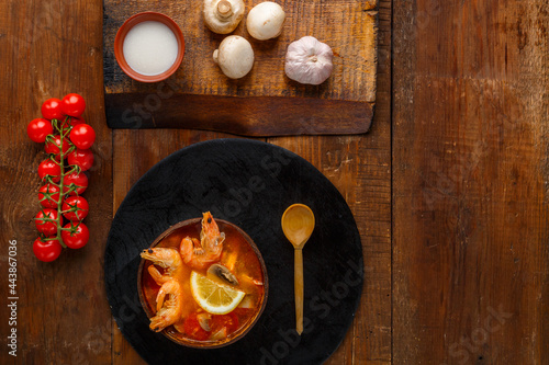 Tom yam soup with shrimps and coconut milk on the table on a round board near milk mushrooms and tomatoes.