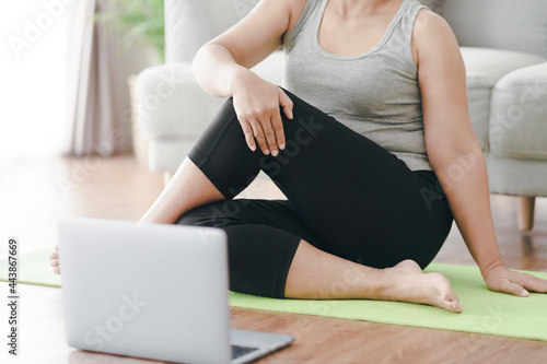 Mature Asian chubby fat woman sitting on the floor in living room practice online yoga lesson with the computer. female having meditate training class on the laptop..