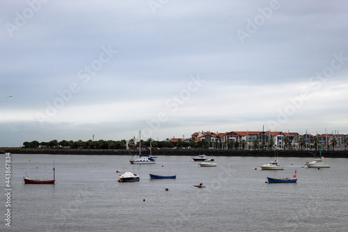 calm sea in a port, small boats are seen under a cloudy sky. houses on the coast