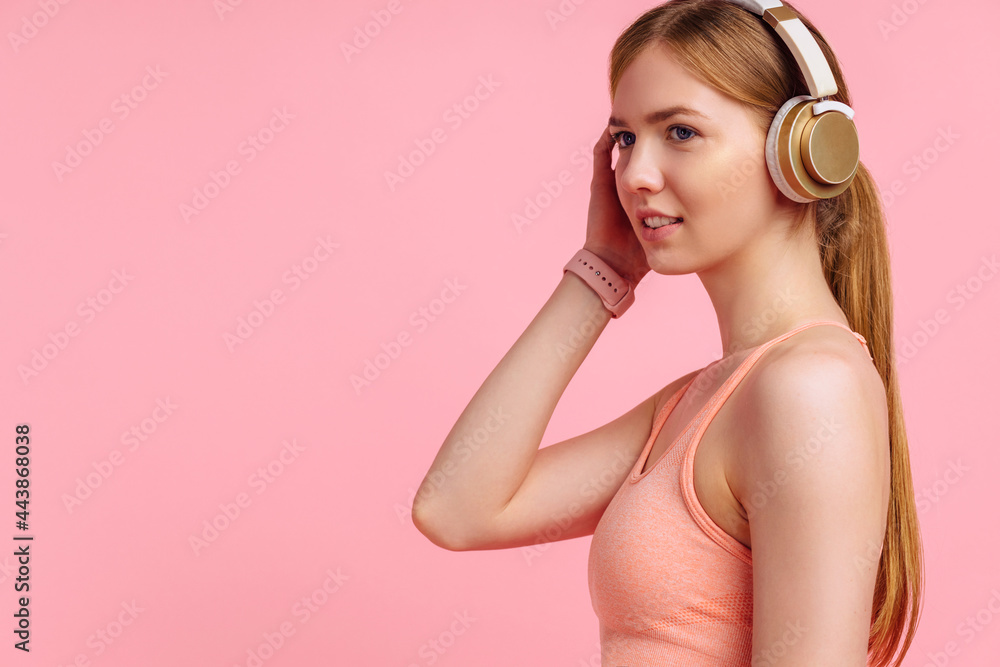 Fitness woman in sportswear relaxing in headphones after workout, on pink background