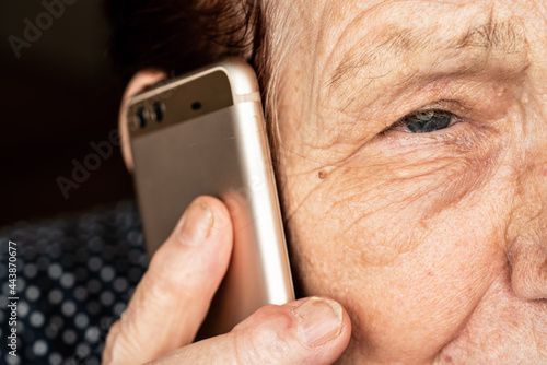 Elderly senior woman holding gold coloured phone next to her ear, closeup detail, only half face visible photo