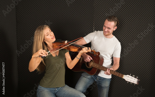 Portrait of a handsome man musician plays the guitar, a beautiful woman musician plays the violin in the recording studio.