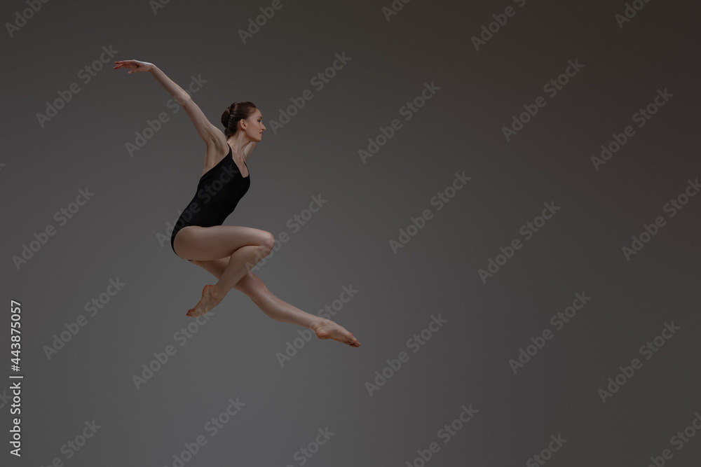 Professional leaping ballerina dancing against gray background