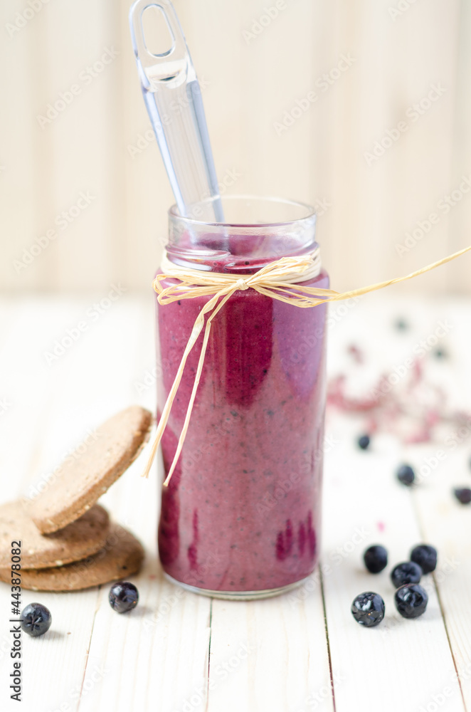 Cranberry and black currant smoothie in glass jars with cookies on a white wooden background