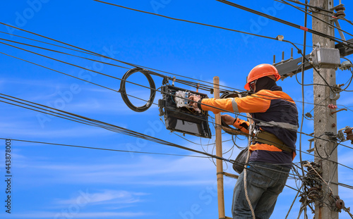 Low angle view of technician on wooden ladder is installing fiber optic system in internet splitter box on electric pole against blue sky background photo