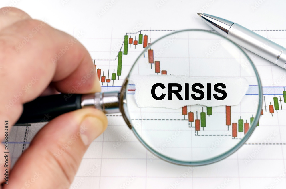 A man looks through a magnifying glass at charts and paper with the inscription - Crisis A man looks through a magnifying glass at charts and paper with the inscription - Crisis