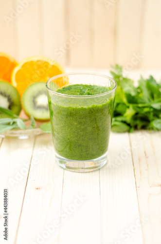 Healthy green smoothie with spinach, kiwi and orange in a glass on light wooden table