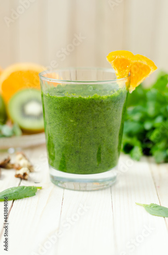 Healthy green smoothie with spinach, kiwi and orange in a glass on light wooden table