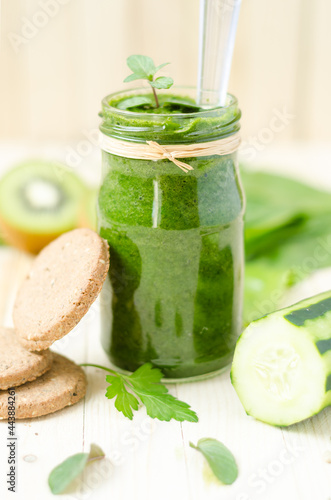 Healthy green smoothie with spinach, kiwi and orange in a retro jar on light wooden table. Integral biscuits and cucumber in the foreground, kiwi in the background.