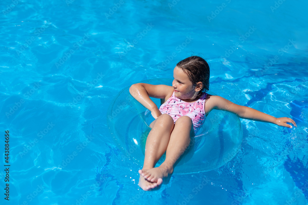 a happy, joyful girl in a pink swimsuit is chill on a transparent inflatable circle in the swimming pool of the hotel on a summer vacation. 