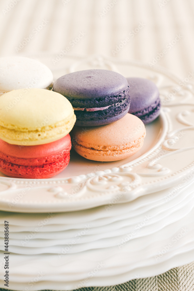 Different coloured macarons on stack of plate on white cake pedestal. Selective focus Different coloured macarons on stack of plate on white cake pedestal. Selective focus