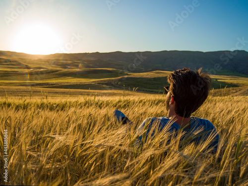 
young man with glasses lying down against the sun in a yellow wheat field, selective focus