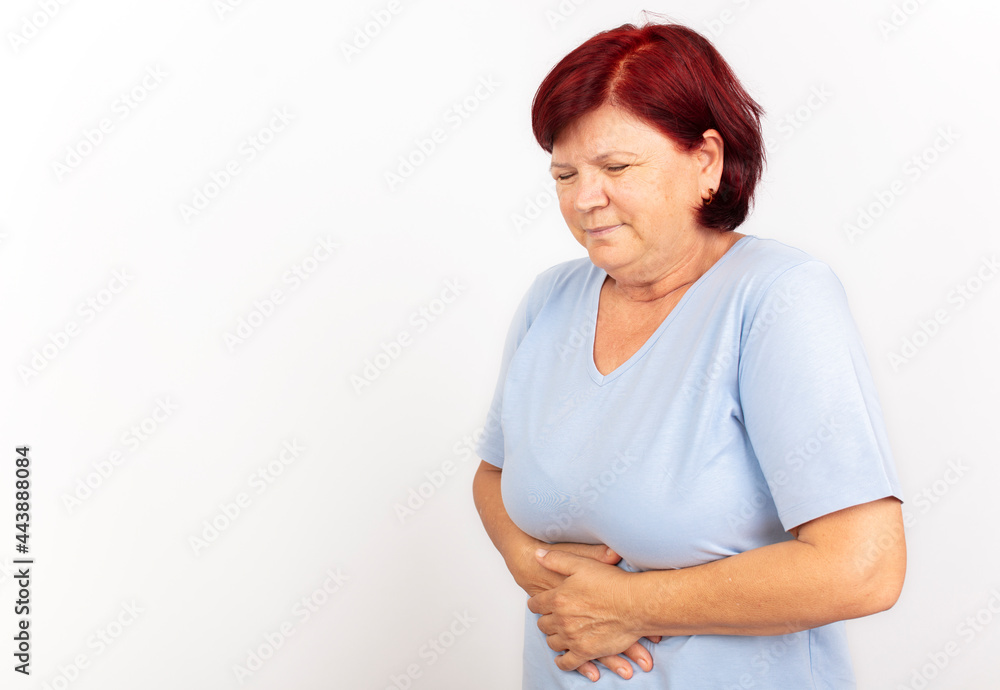 Mature woman experiencing stomach pain and cramps against a white background Mature woman experiencing stomach pain and cramps against a white background