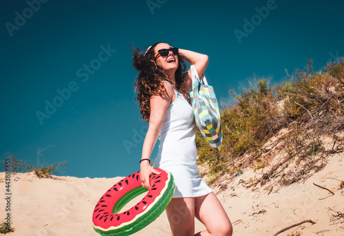Girl with bag and rubber ring on beach. Young woman having fun walking along the sandy beach in the summer.