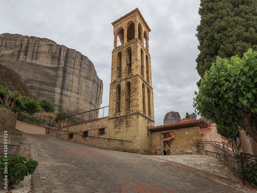 The tall elegant bell tower on a hill in front of a pillar-like huge rocky mountain, Kalambaka, Meteora, Greece