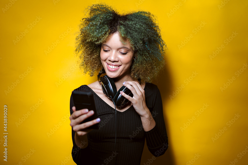 afro woman watch her phone and smiles on yellow background afro woman watch her phone and smiles on yellow background
