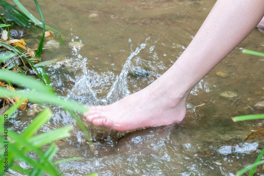 Young boy playing barefoot with clear water at a little creek using his feet and the water spring cooling his toes and legs and refreshing with the pure elixir of life in zen meditation atmosphere Young boy playing barefoot with clear water at a little creek using his feet and the water spring cooling his toes and legs and refreshing with the pure elixir of life in zen meditation atmosphere