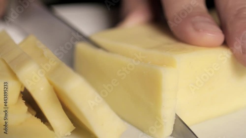 knife cutting block of cheese into slices close up
