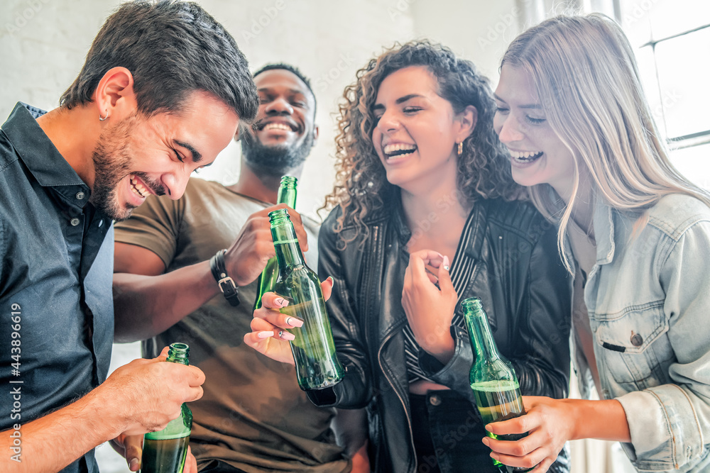 Group of friends laughing and holding beer bottles indoors.