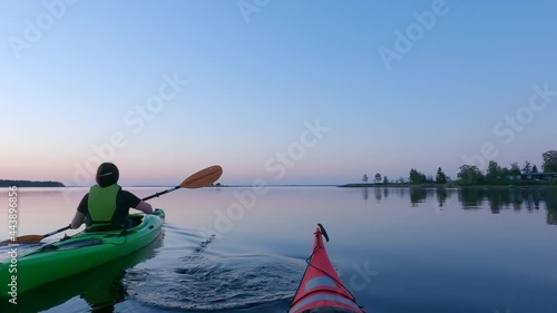 Girl kayaking and then taking break from paddling, looking at mobile phone, mirror like calm water at midnight in Northern Sweden during light Summer night Sun in polar regions. Umea, Sweden.