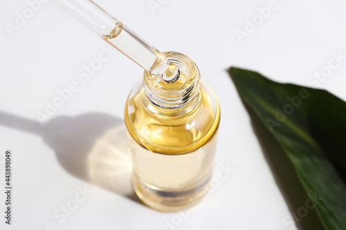 Bottle of cosmetic essential oil and green leaf. Serum oil is dripping from dropper. Close-up. Beauty and body care concept. Serum skin care product. Hard light photo