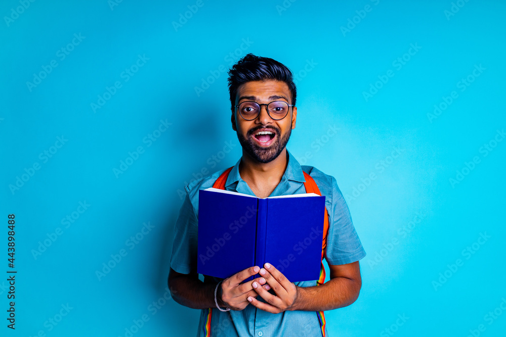 handsome young bearbed indian man with eye glasses in blue cotton t-shirt with orange rainbow backpack in studio background handsome young bearbed indian man with eye glasses in blue cotton t-shirt with orange rainbow backpack in studio background