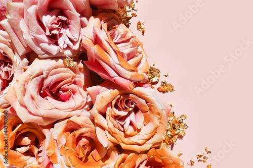 Pink gold roses and pieces of golden paper on powdery pink background. Cosmetics product advertising backdrop or background. Empty place to display product packaging. Mockup, copy space.