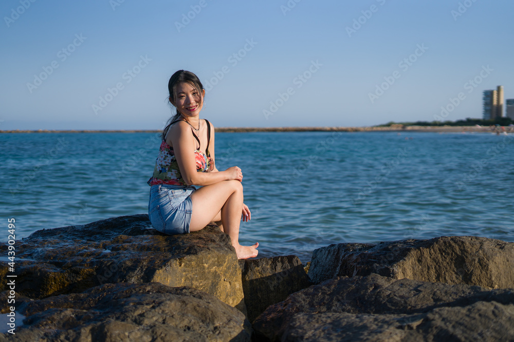 young Asian woman by blue sea -  happy and beautiful Chinese girl  enjoying holiday trip relaxed and cheerful at beach rock cliff during summer in tourist  travel concept