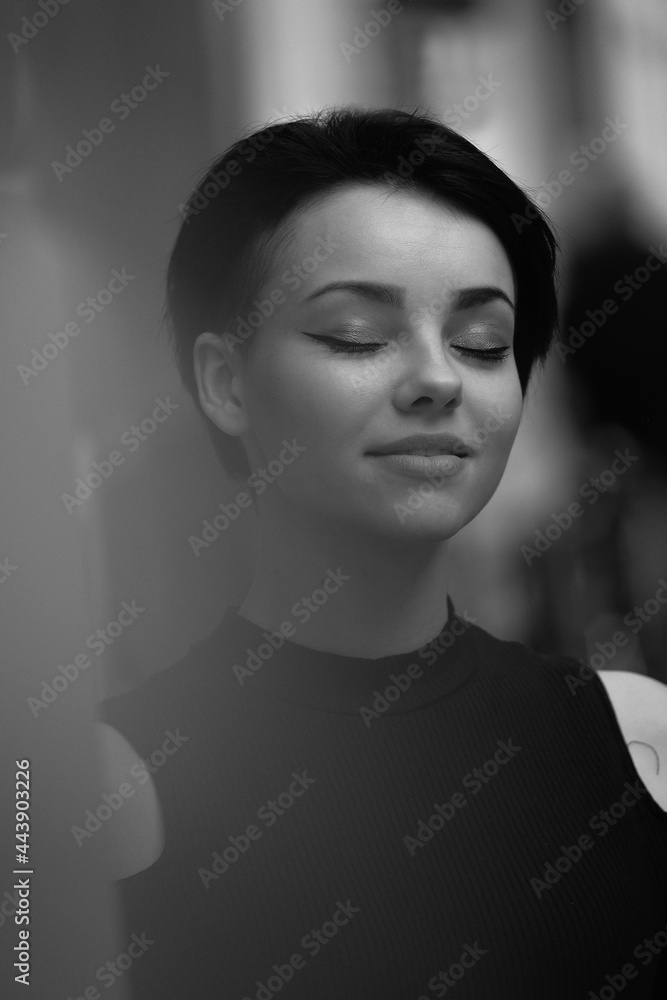 Black and white portrait of a happy young girl in the city. Short hair, a sincere smile and closed eyes. Beautiful woman in classic black clothes Black and white portrait of a happy young girl in the city. Short hair, a sincere smile and closed eyes. Beautiful woman in classic black clothes