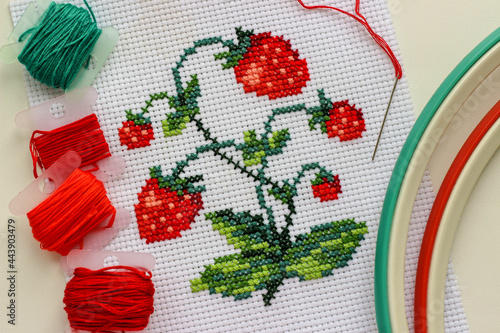 Red ripe strawberries embroidered with a cross-stich on a white canvas by hand. With a needle, thread floss and hoop.