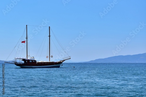 Seascape. Two-masted sailboat in sea bay on sunny day against background of mountains and blue sky