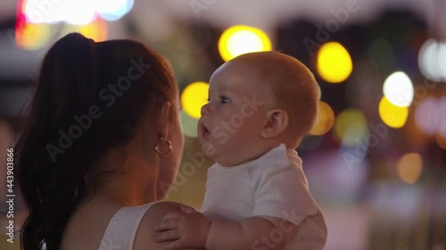 Mom and baby in the night amusement park. Holds an emotional child in her arms for the first time in the luno park, with lots of lights in the background out of focus photo