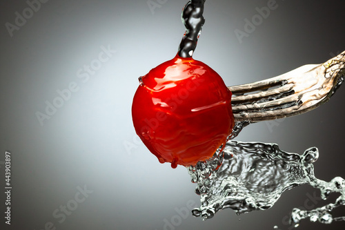 red cherry tomato on a silver fork. A jet of water, splashes of water. Black white gradient background. Place under the text