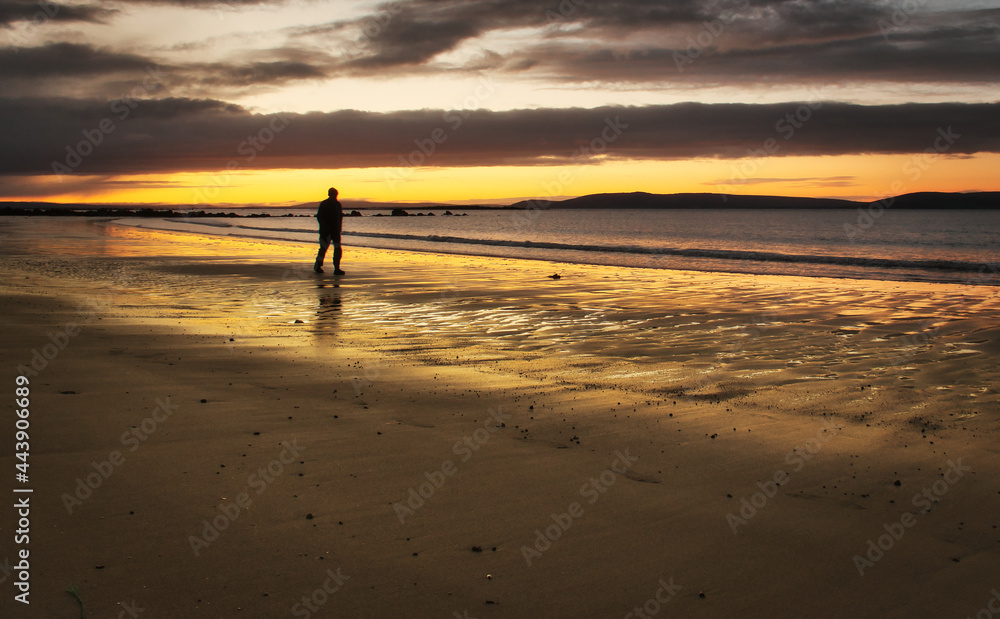 Beautiful morning orange sunrise with silhouetted man walking down the beach at Silverstrand, Galway, Ireland 