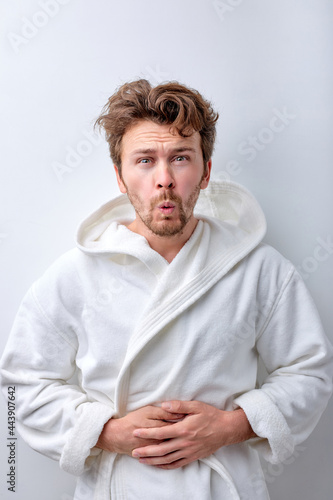 Young bearded adult man wearing bathrobe with hand on stomach because indigestion, painful illness feeling unwell. Ache concept. Isolated white studio background, copy space. People human emotions © Roman