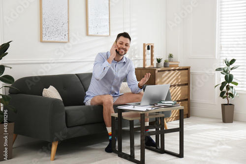 Businessman in shirt and underwear talking on phone while working with laptop at home