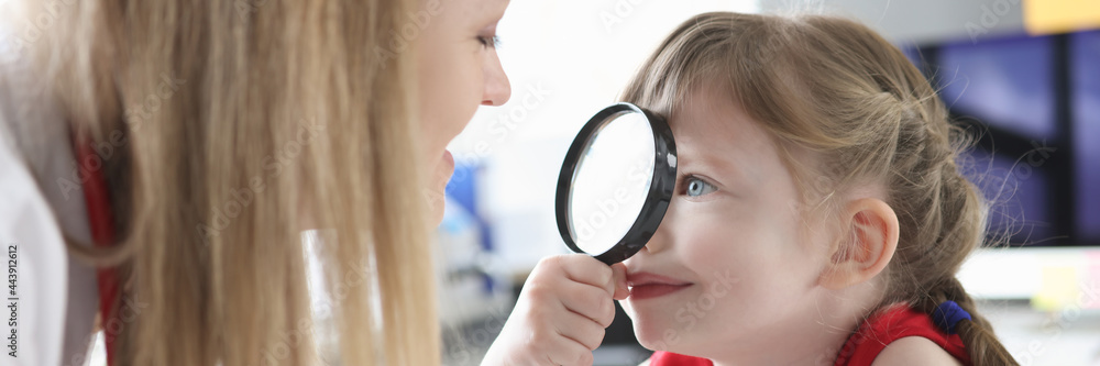 Little girl looking at pediatrician doctor with magnifier in clinic Little girl looking at pediatrician doctor with magnifier in clinic