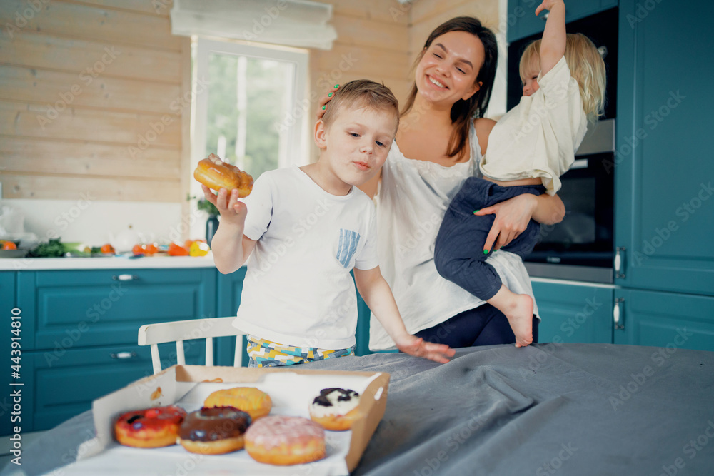 Eat sweet dessert doughnuts on delivery to the house. Young family smiling mother and children in the kitchen. Happy time together with your family, good mood.